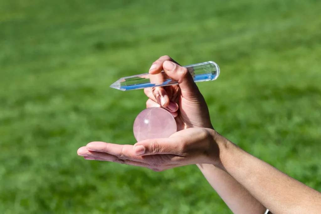 Hand holding a rose quartz crystal and a clear crystal wand outdoors