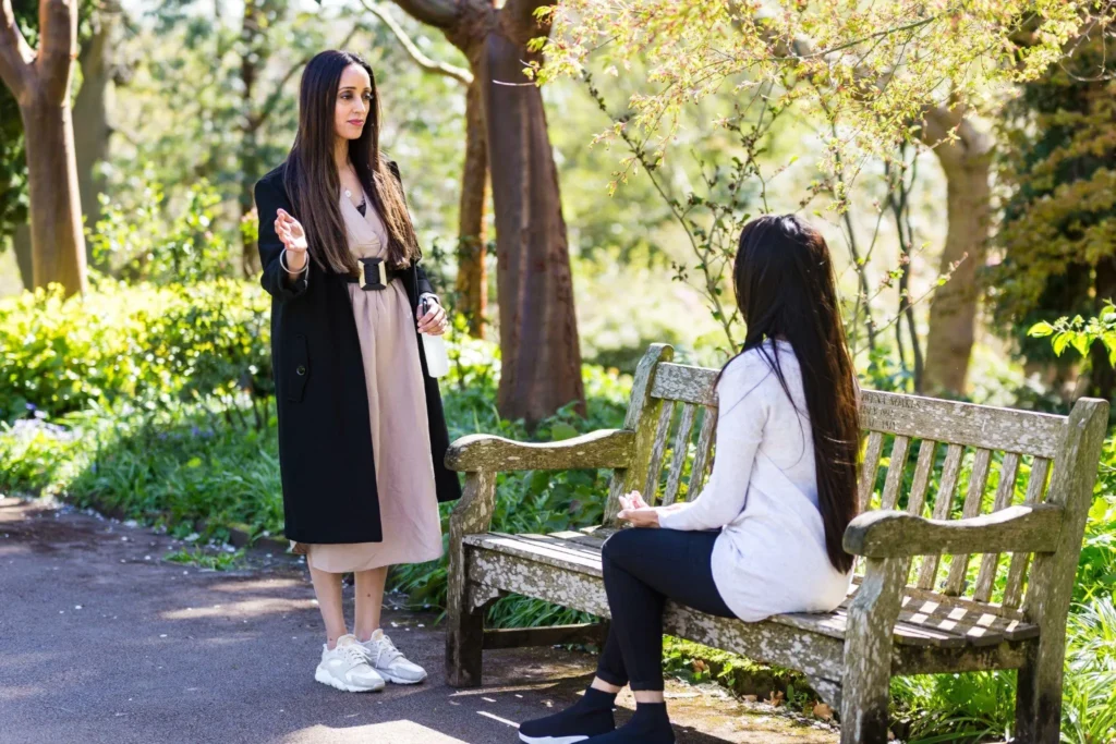 Two women talking on a park bench among trees