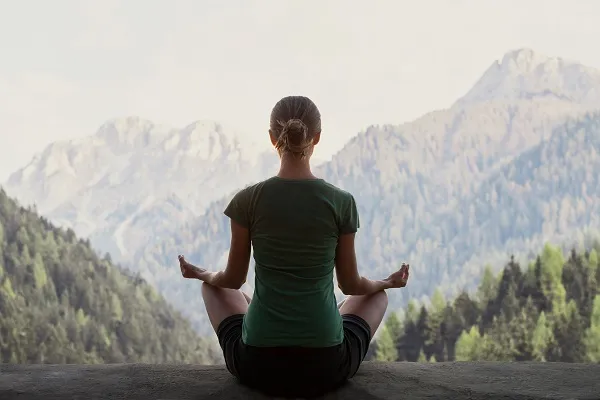 Woman meditating cross-legged facing mountains