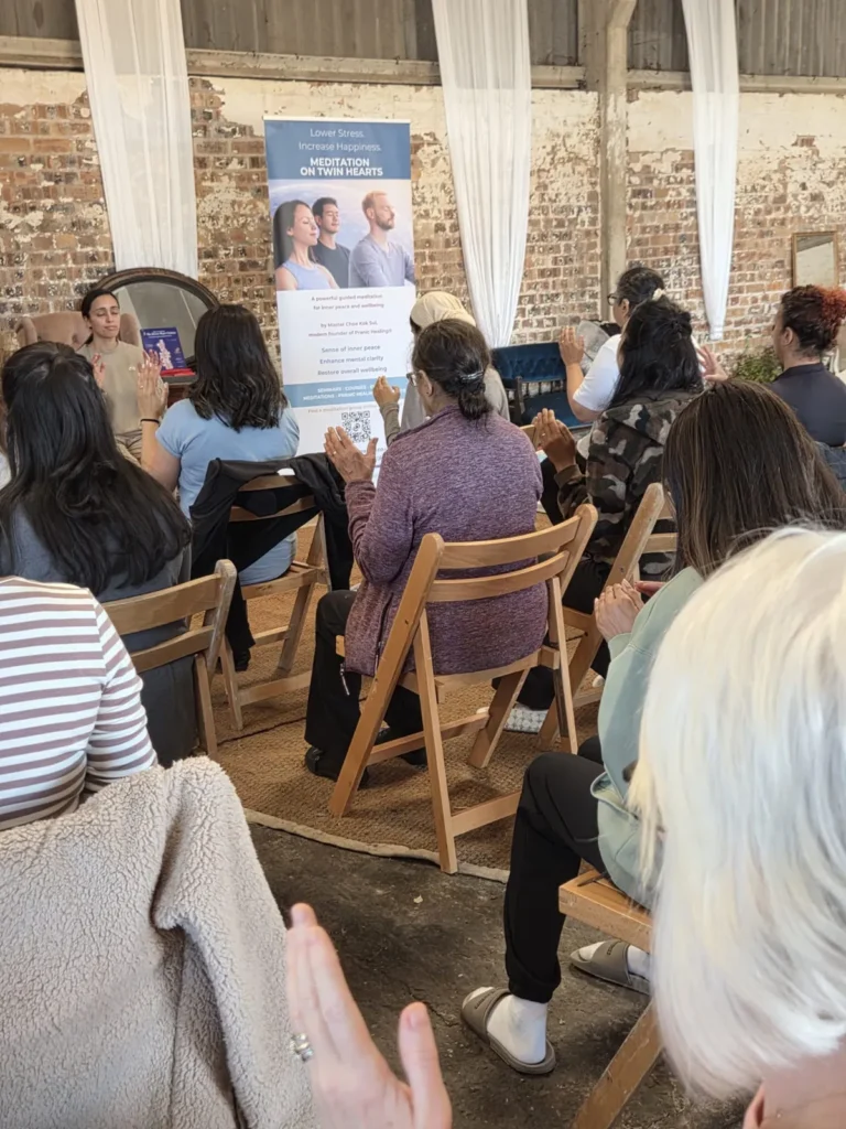 Participants seated on chairs with hands raised during Meditation on Twin Hearts
